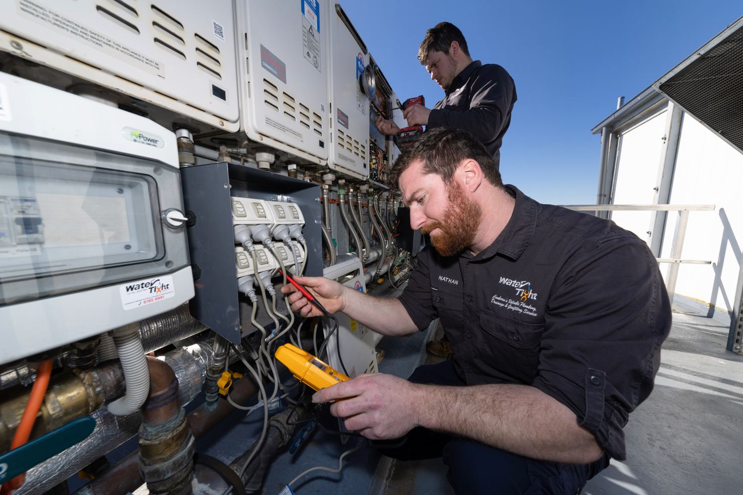 Water Tight technicians testing electrical connections on Rheem commercial hot water units during a scheduled preventative maintenance service